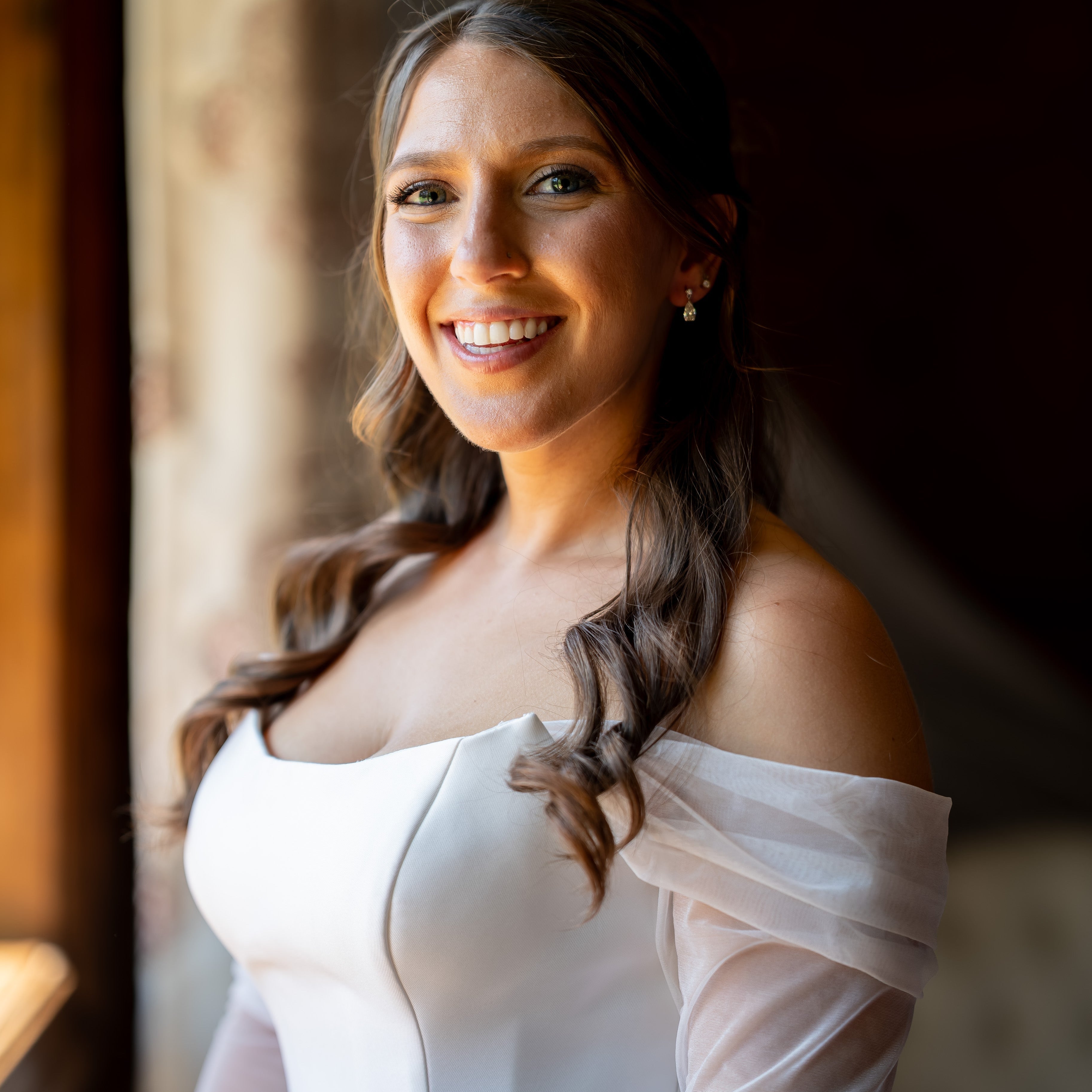 Woman in a white off-shoulder dress standing indoors with a blurred background