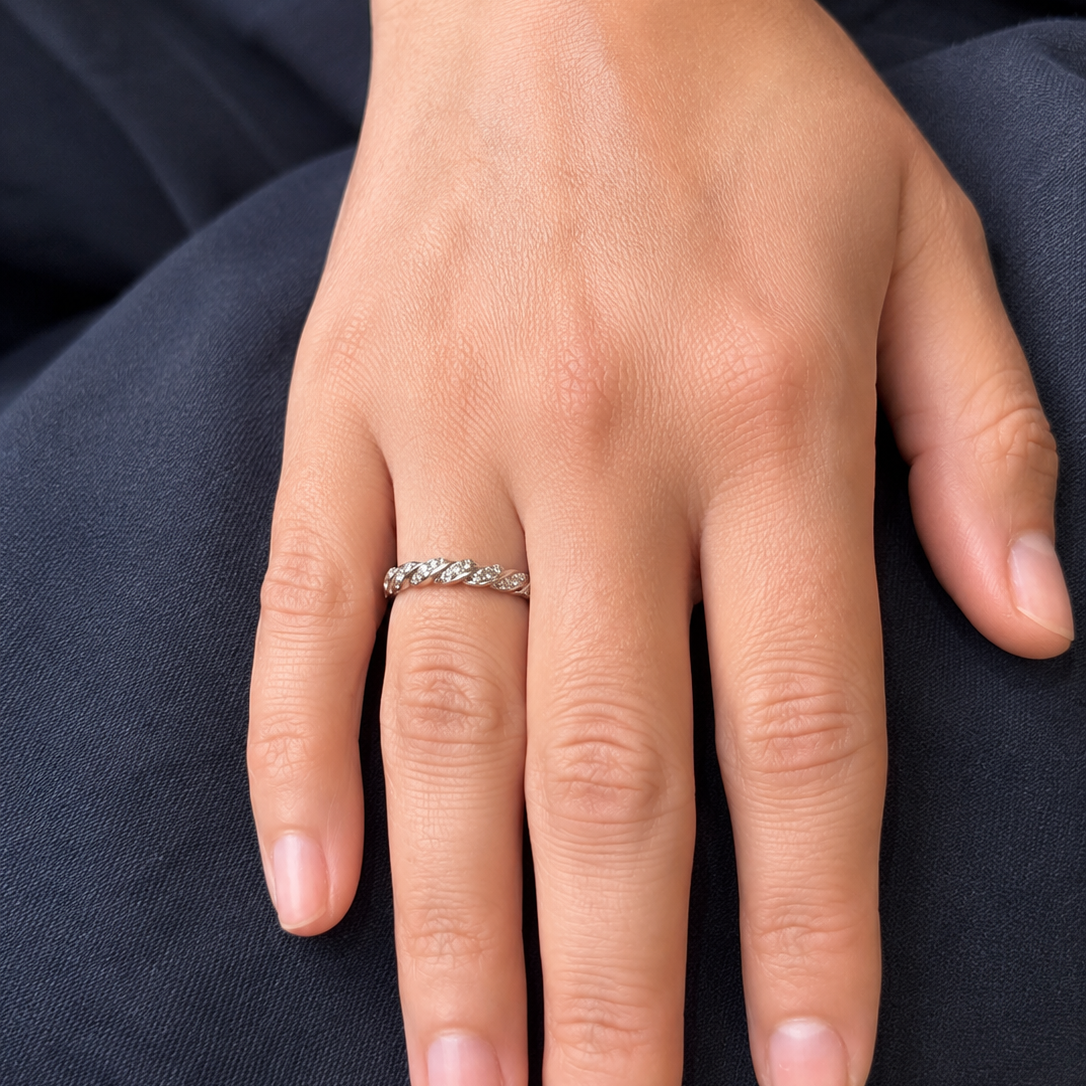 A close-up of a person's hand resting on dark navy fabric, wearing a thin silver band ring with small clear stones.